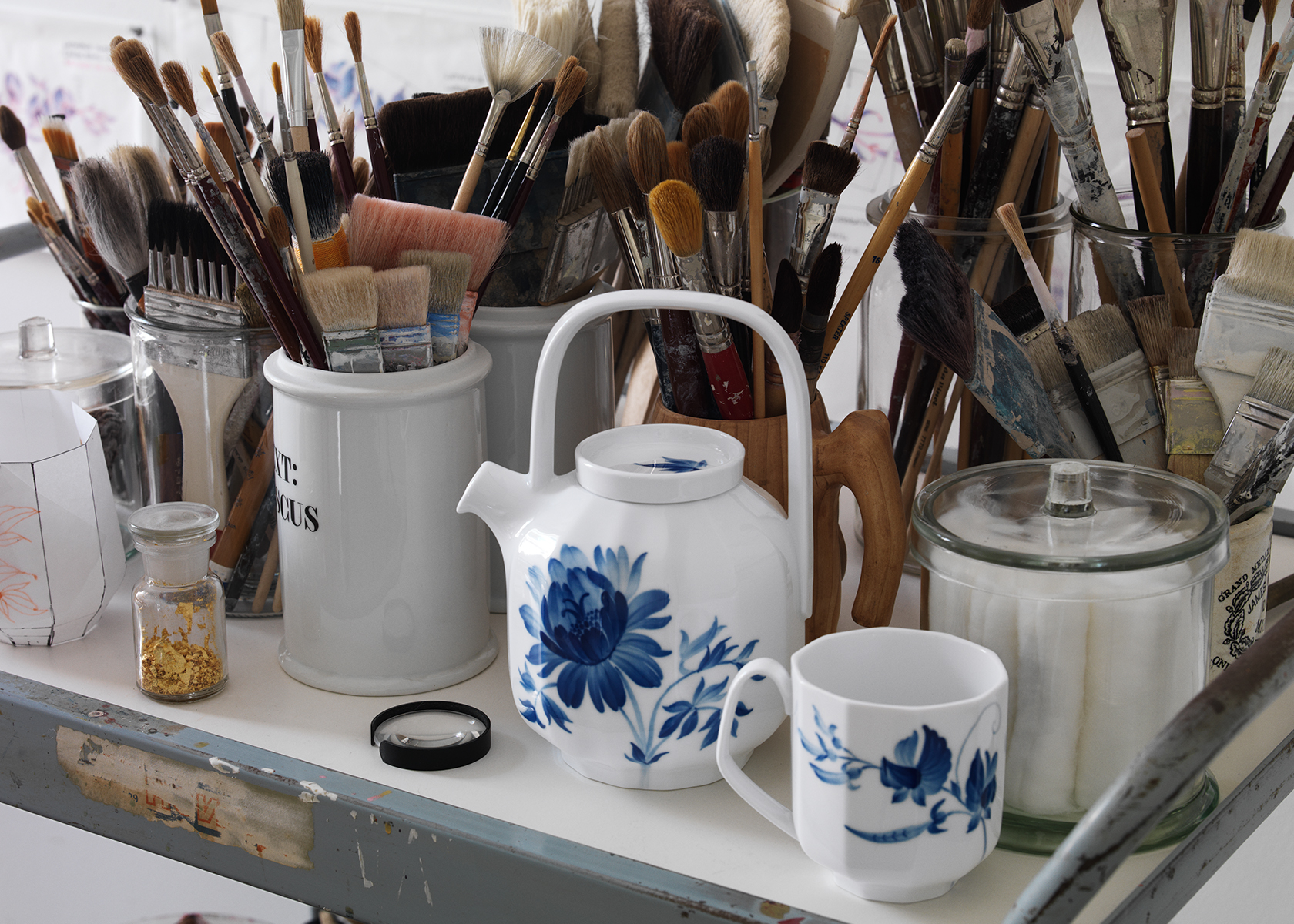 blomst teapot and mug on a table next to a lot of paint brushes in an atelier